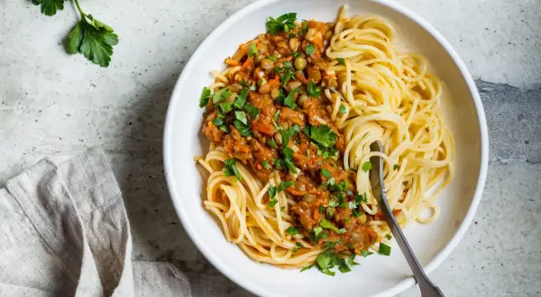 Porcja spaghetti z sosem z soczewicy i warzyw, posypana natką pietruszki. Zdjęcie sugeruje zdrowe spaghetti kcal.