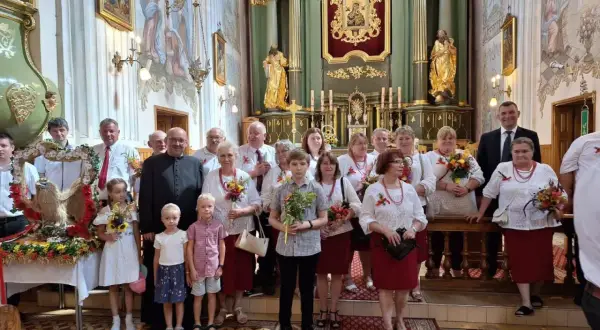 Uroczystość Wniebowzięcia Najświętszej Maryi Panny w kościele. Grupa osób w strojach ludowych i duchowny pozują do zdjęcia.