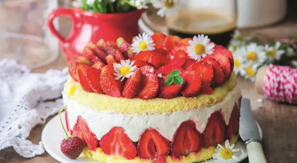 Puszysty biszkopt z truskawkami i mascarpone, ozdobiony świeżymi owocami i stokrotkami. Idealny na letnie popołudnie.
