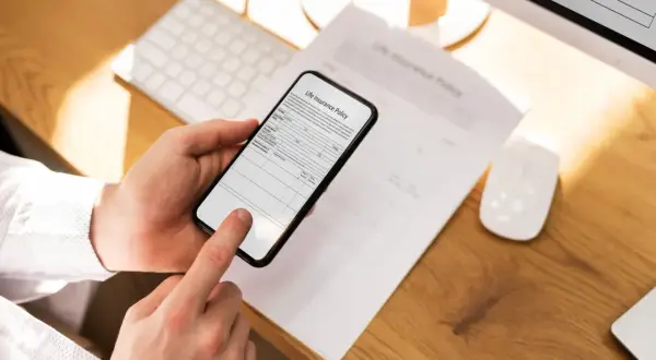 Ręce trzymają telefon, który działa jak skaner w telefonie, skanując dokument "Life Insurance Policy".