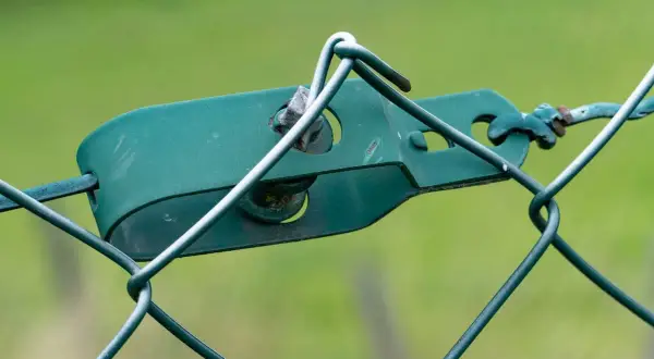 Grüner Drahtspanner hält den Maschendrahtzaun straff.