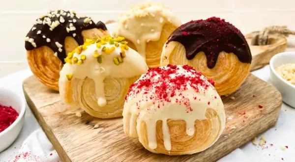 Fünf köstliche New York Rolls, verlockend mit Schokolade, Pistazien und roten Streuseln verziert, auf einem Holzbrett.