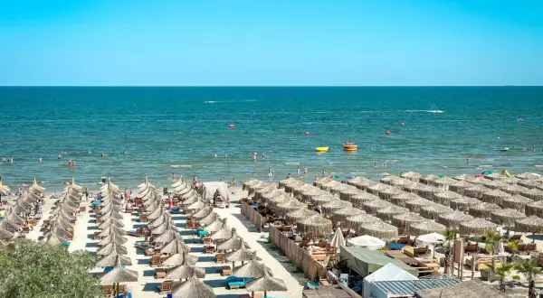 Słoneczne rumuńskie wakacje nad Morzem Czarnym. Plaża pełna leżaków i parasoli, ludzie kąpią się i relaksują.