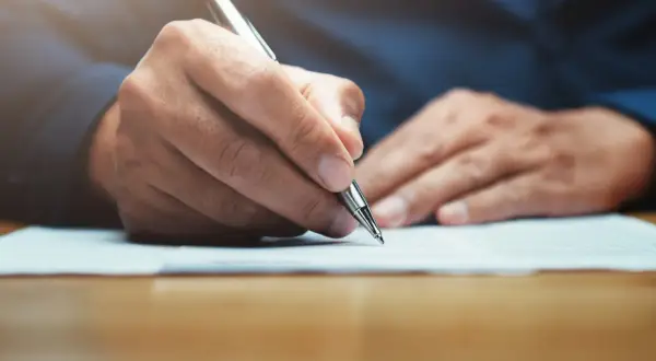 Main tenant rédigeant une lettre, peut-être un modèle lettre CARSAT, avec un stylo argenté sur un document.