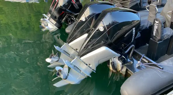 Motori fuoribordo Mercury Verado, con eliche lucide che riflettono l'acqua verde. L'alto bordo del gommone è visibile, pronto per la navigazione.