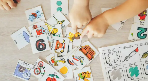Manos de niños jugando con tarjetas de aprendizaje, practicando ejercicios de memoria con imágenes de animales, números y objetos.