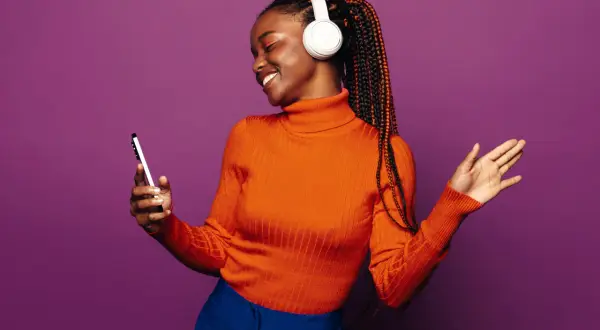A woman with braids and headphones smiles, holding a phone. She's a visual representation of how to get your music on playlists.