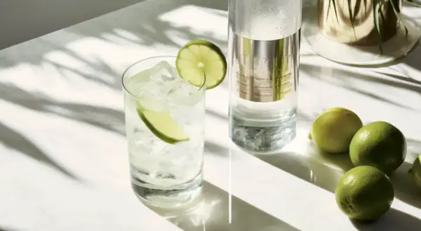 Szklanka z wódką i lodem, plasterkami limonki, butelka wódki i kilka limonek na marmurowym blacie.