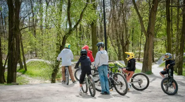 Grupa dzieci w kaskach odpoczywa na rowerach na bielszowice trails. W tle widać leśną ścieżkę rowerową.