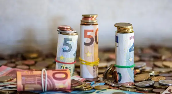 Zrolowane banknoty euro (5, 10, 50) z monetami na górze i wokół. To może być zgłoszenie darowizny od rodziców.