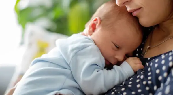 Mutter hält ihr schlafendes Baby. Der leichte baby haarausfall ist kaum sichtbar, während das Kind friedlich an ihrer Brust ruht.