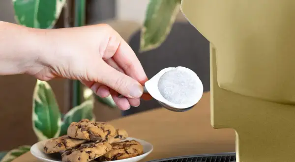 Una mano inserisce una cialda ese, perfetta per un caffè veloce, accanto a biscotti al cioccolato.