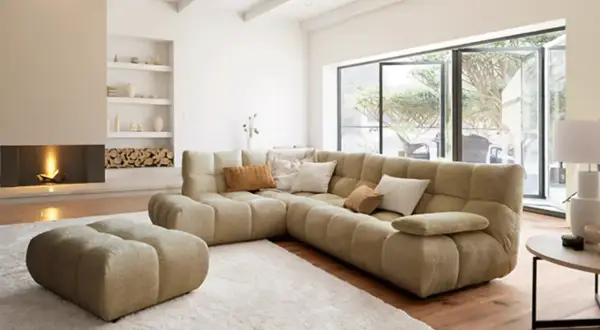 Gemütliches Wohnzimmer mit großem Ecksofa, Kamin und Blick in den Garten – ein Ausblick auf die wohntrends 2026.