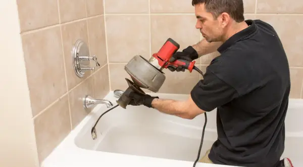 Plombier utilise un furet électrique pour comment déboucher une canalisation dans une baignoire.