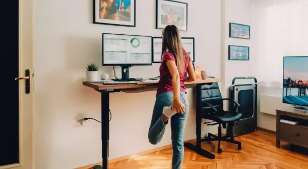 Une femme s'étire près d'un bureau réglable en hauteur, parfait pour faire un bureau avec un plan de travail ergonomique.