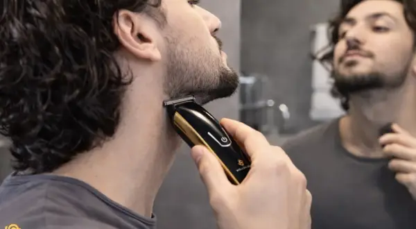 Un homme ajuste sa barbe 3mm avec une tondeuse dorée et noire devant un miroir.