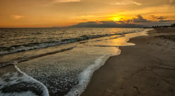 Zachód słońca na plaży w Turcji w październiku. Fale delikatnie obmywają piaszczysty brzeg, a niebo mieni się odcieniami złota i pomarańczy.