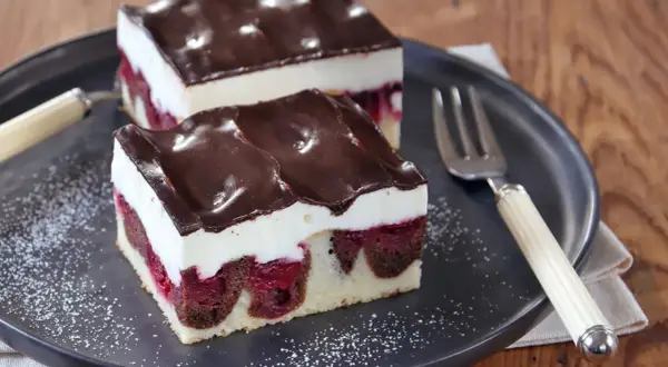Zwei Stücke saftige Donauwelle mit Kirschen, weißer Creme und Schokoladenguss auf einem Teller. Ein köstliches Donauwelle Rezept!
