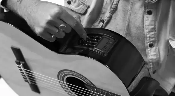 Dłoń z pierścionkami reguluje pokrętła na gitarze, przygotowując się do nauki gry na gitarze elektrycznej.