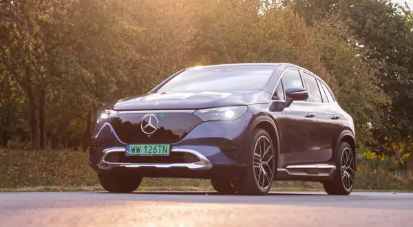 Elegancki, ciemnogranatowy Mercedes EQE SUV lśni w jesiennym słońcu na tle drzew.