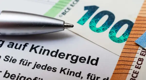 Długopis nad dokumentem o Kindergeld w Niemczech, obok banknotów 100 i 50 euro.