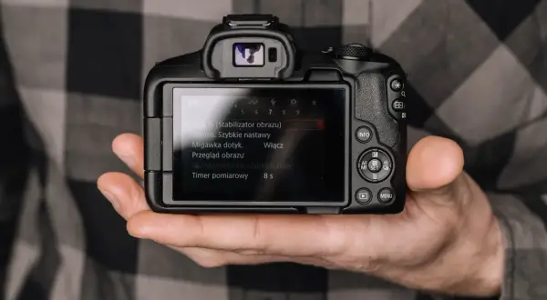 Dłoń trzyma aparat, na ekranie menu. Minimalizm w fotografii to sztuka uchwycenia esencji.