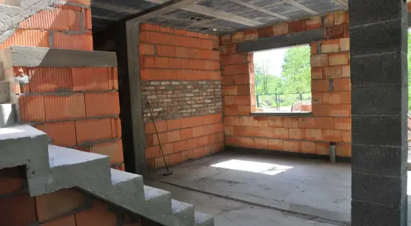 Wnętrze w budowie, widoczne schody i ściany z pustaków ceramicznych. Trwa samowolne przekształcenie budynku gospodarczego na mieszkalny.