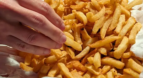 En hand plockar en gyllene pommes frites ur en stor hög med krispiga pommes frites.