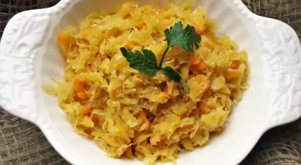 Pyszna kapusta kiszona gotowana z marchewką, udekorowana natką pietruszki, podana w białej miseczce.