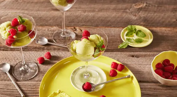 Erfrischendes Kiwi-Sorbet mit Himbeeren und Minze in eleganten Gläsern auf Holzhintergrund.