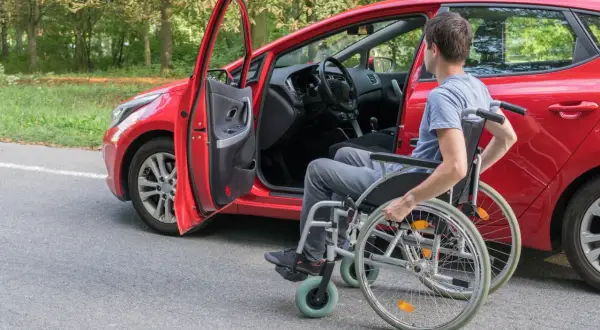 Uomo in carrozzina accanto a un'auto rossa, pronto per il passaggio di proprietà auto disabile decesso.