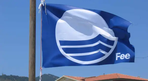 Bandiera blu con logo FEE sventola su un cielo azzurro, simbolo di qualità ambientale.