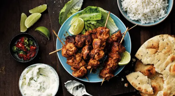 Tandoori kyckling på spett, serverad med ris, naanbröd, raita och limeklyftor.