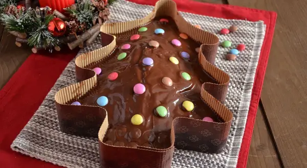Dolce a forma di albero di Natale ricoperto di glassa al cioccolato e decorato con caramelle colorate.