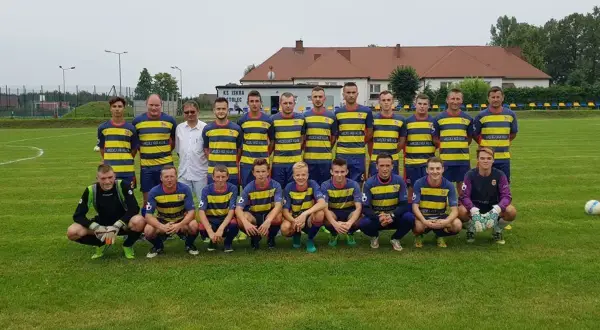 Drużyna KS Iskra Stolec gotowa do meczu. Piłkarze w żółto-niebieskich strojach, jeden w bramkarskim.