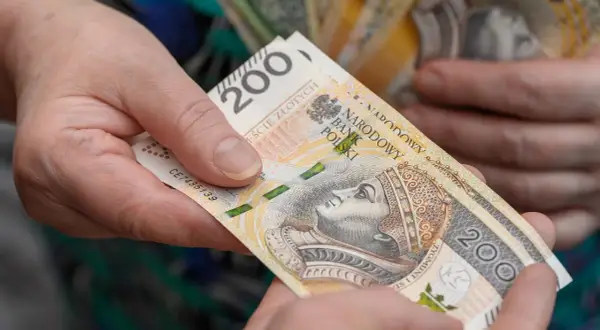 Dwie dłonie przekazują sobie banknot 200 zł. Czy wychowanie dzieci liczy się do emerytury?