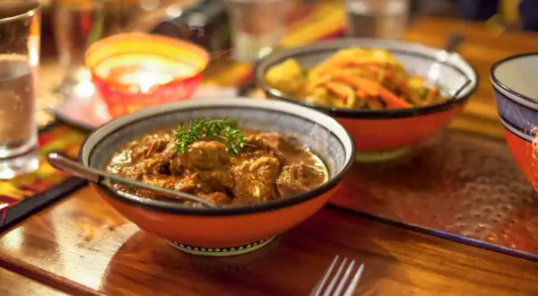 En skål med mustig gryta, en klassiker inom sydafrikansk mat, serveras med en gaffel. I bakgrunden syns en annan skål med grönsaker och en flammande ljuslykta.