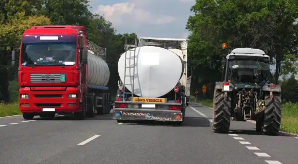Czerwona ciężarówka próbuje wyprzedzanie na trzeciego, omijając traktor i inną cysternę na wąskiej drodze.