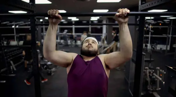Uomo con fisico endomorfo si allena in palestra, concentrato su una trazione alla sbarra.