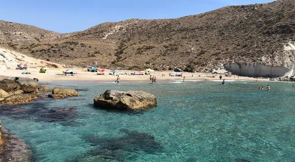 Aguas cristalinas en la cala del medio, con gente disfrutando del sol y el mar en un día soleado.