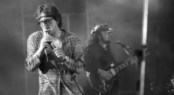 Wokalista z opaską na głowie i w kratę śpiewa do mikrofonu, obok gitarzysta. Widać, że perfect wszystko ma swój czas, nawet na scenie.