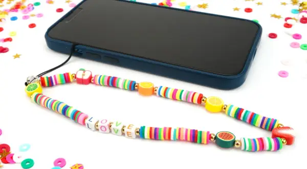 Comment faire un bracelet de téléphone : un cordon coloré avec des perles fruits et lettres "LOVE" est attaché à un smartphone.