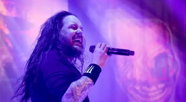 Jonathan Davis z zespołu Korn śpiewający do mikrofonu na fioletowej scenie.