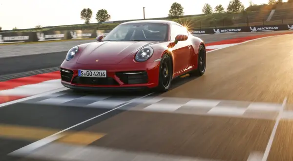 Czerwone Porsche 911 GTS sunie po torze wyścigowym, odbijając promienie zachodzącego słońca.