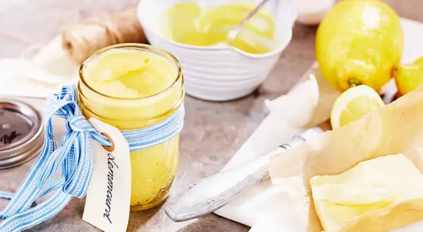 En burk med krämig lemon curd, redo för ett recept. Citroner och smör ligger bredvid.