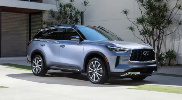 Elegancki, srebrny Infiniti QX60 parkuje przed nowoczesnym domem, otoczony bujną zielenią.
