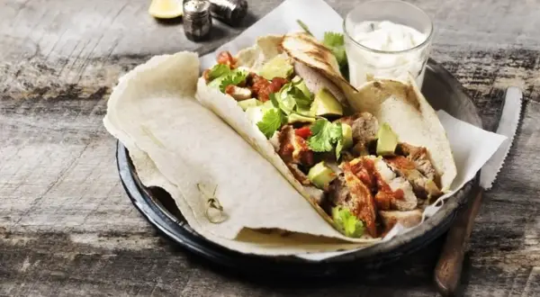 Tortilla z kurczakiem, awokado i sosem na drewnianym stole.