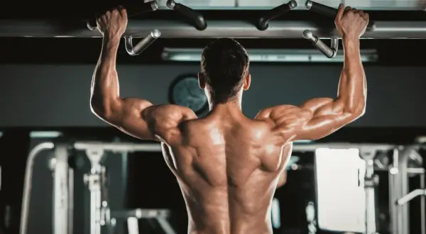 Mężczyzna wykonuje podciąganie na drążku, napinając potężne **biceps**y.