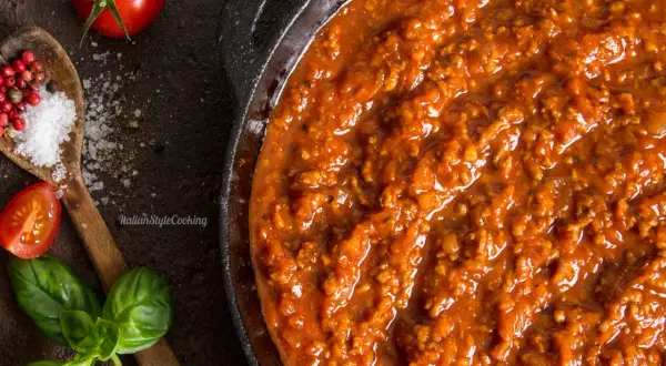 Herzhafte Bolognese-Sauce in einer Pfanne, mit frischen Tomaten, Basilikum, Salz und Pfefferkörnern als Zutaten für Bolognese.