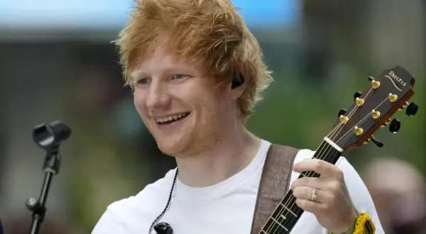 Ed Sheeran gra na gitarze, uśmiechając się do fanów. Jego koncert w Polsce był niezapomnianym przeżyciem.